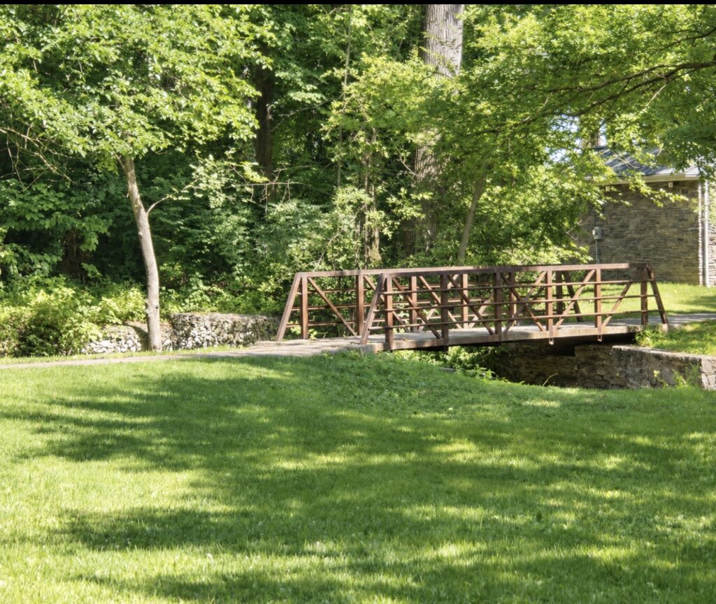 Green lawn, mature trees and a footbridge at Wynnewood Valley Park in Lower Merion, Pennsylvania.